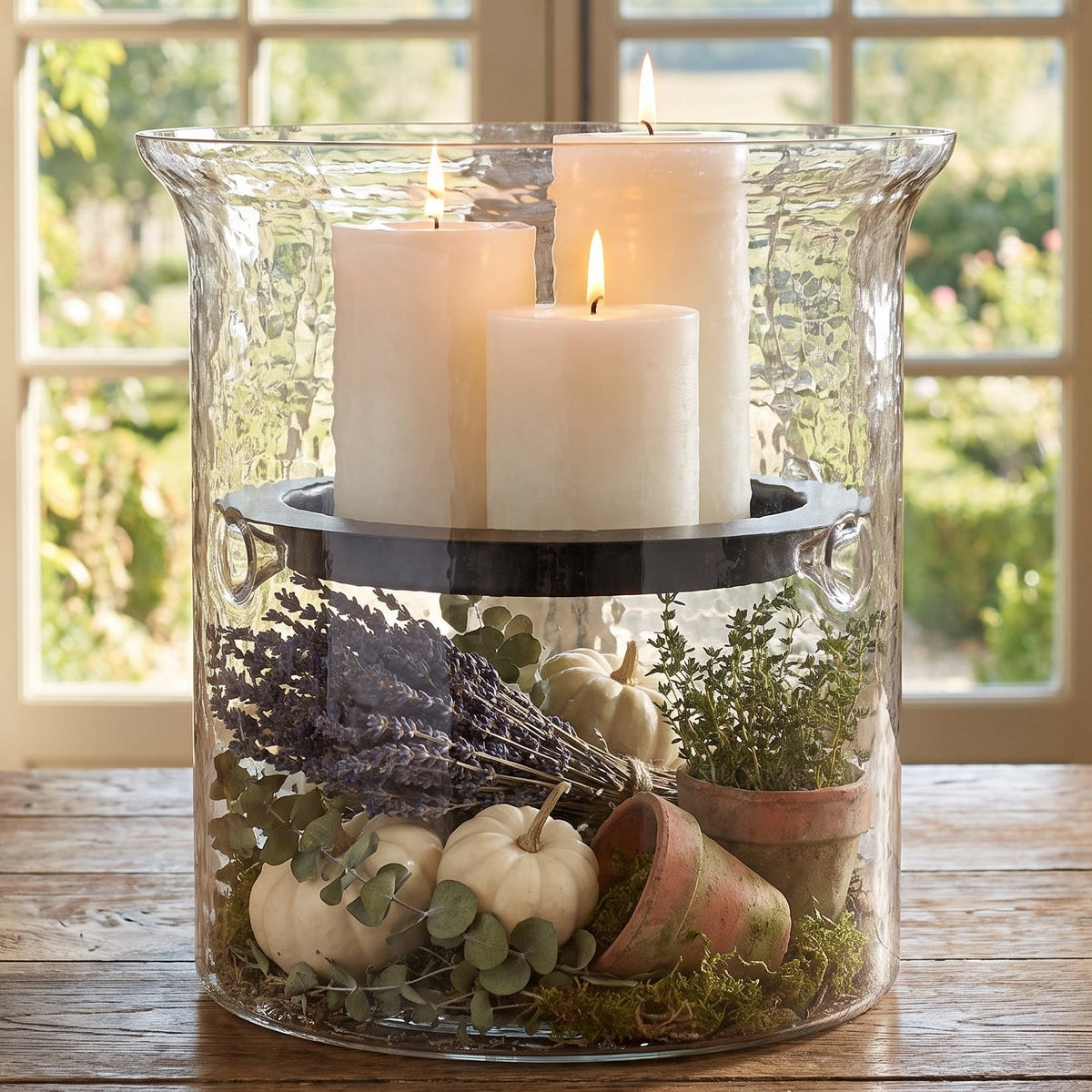 Three white candles in a autumn inspired filled glass centerpiece 