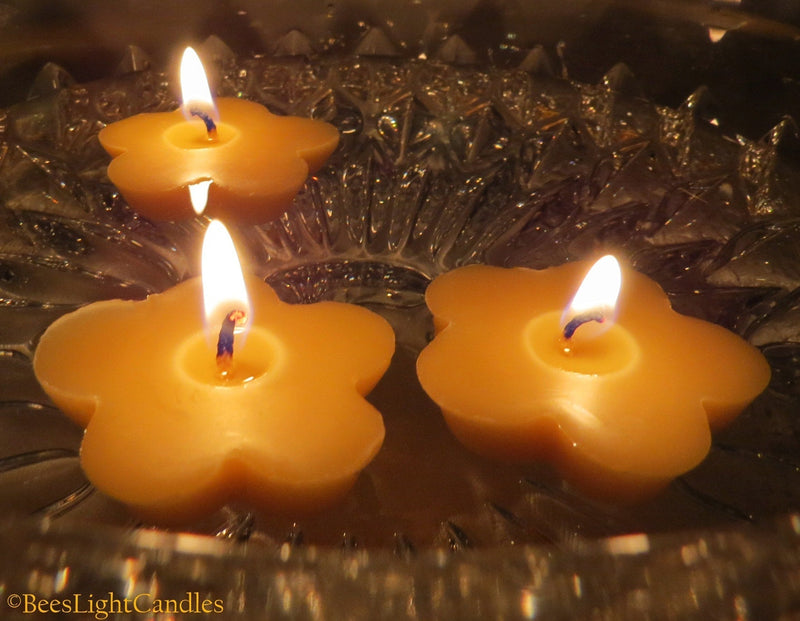 Clover-shaped yellow beeswax floating candles with flames, close-up