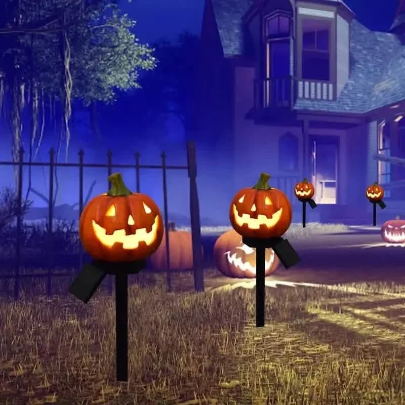 Multiple orange jack-o'-lantern solar stake lights with glowing carved faces by fence
