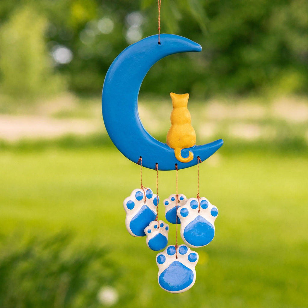Ceramic cat paw wind chime with blue crescent moon and dangling blue paw ornaments outdoors