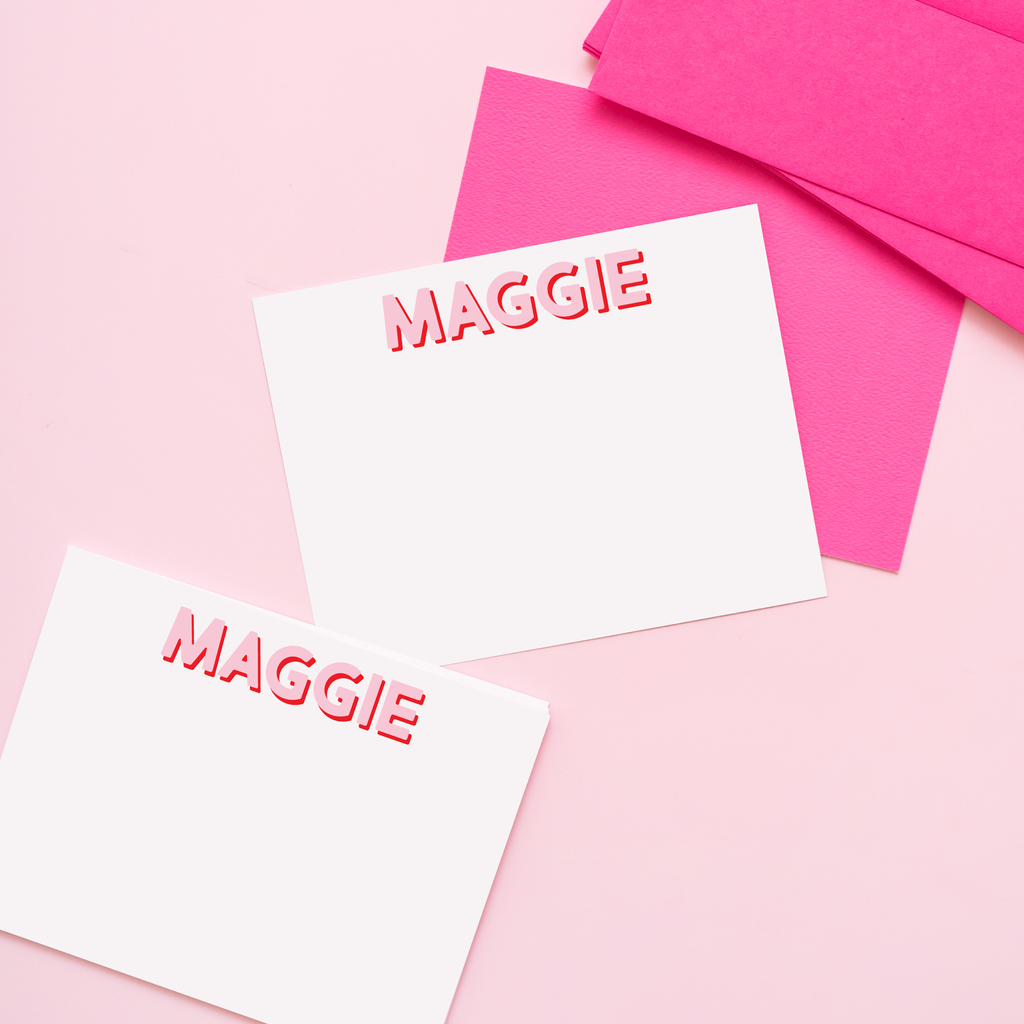 Personalized name cards with “MAGGIE” text on white cards and pink envelopes