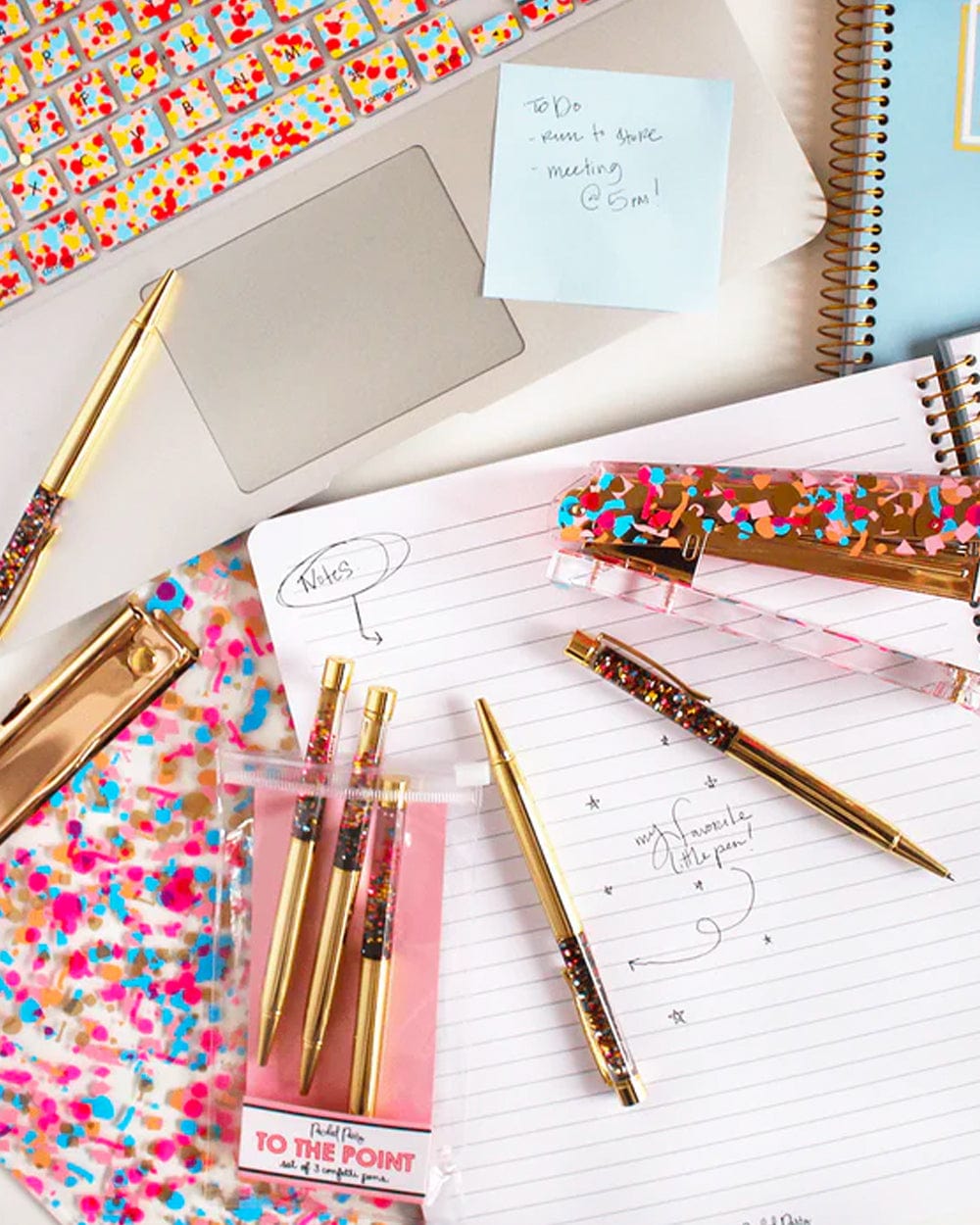 Gold confetti-filled ballpoint pens with metallic caps, shown on a desk