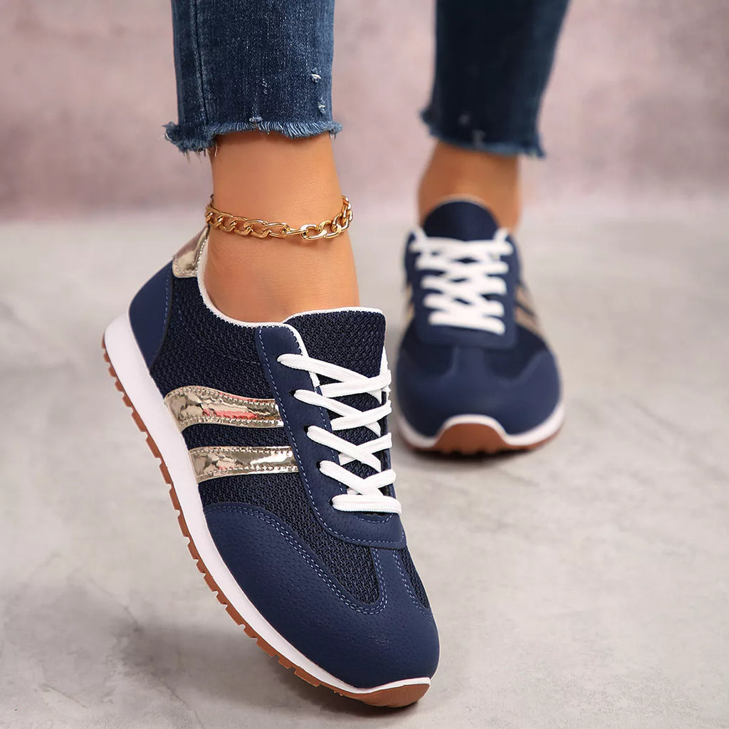 Navy blue lace-up sneakers on feet with gold stripe detailing and white laces