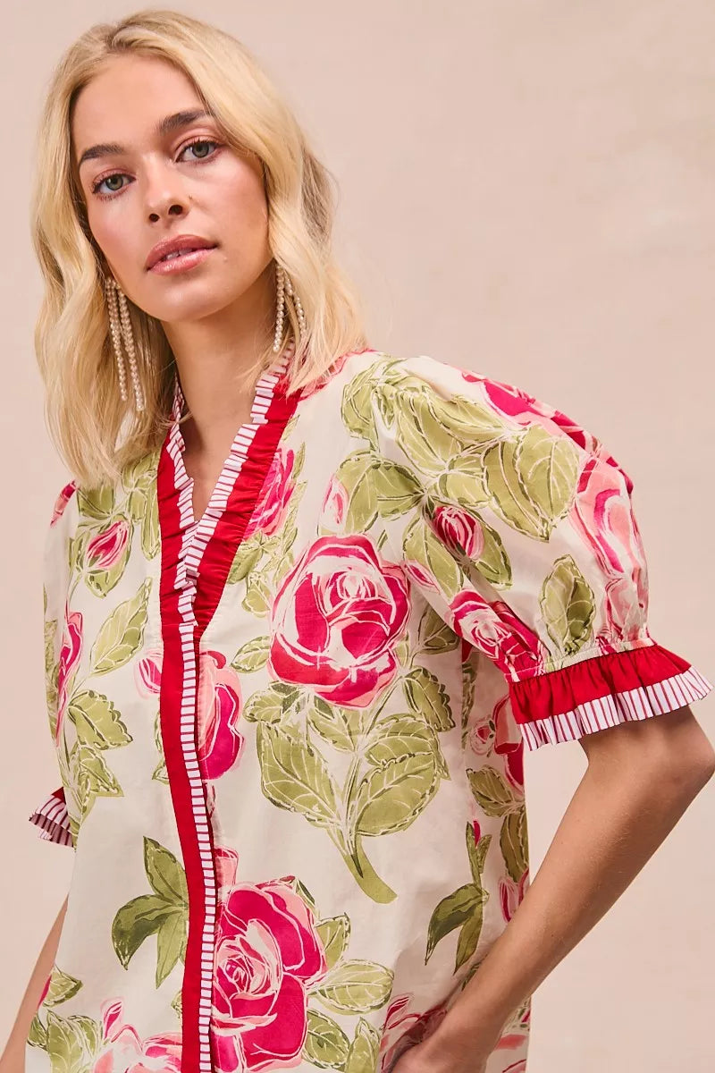 Floral printed blouse detail: coral-trimmed neckline and ruffled sleeve cuff