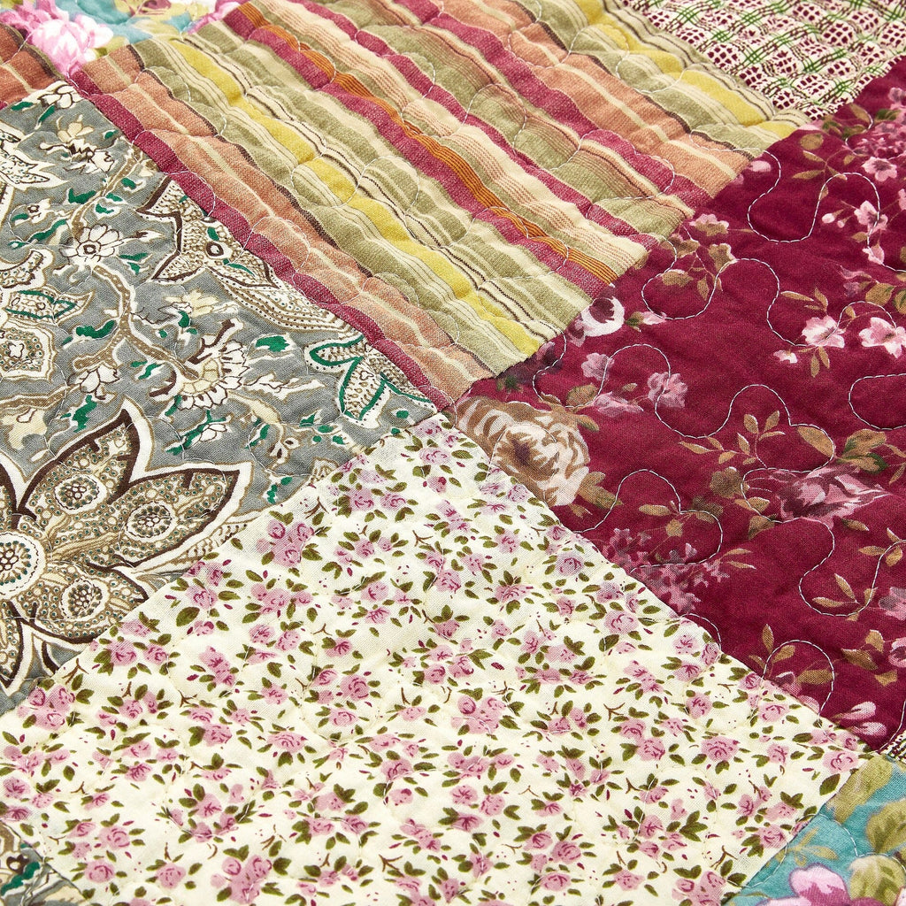 Close-up patchwork quilt with burgundy floral, teal medallion, and multicolor stripes.