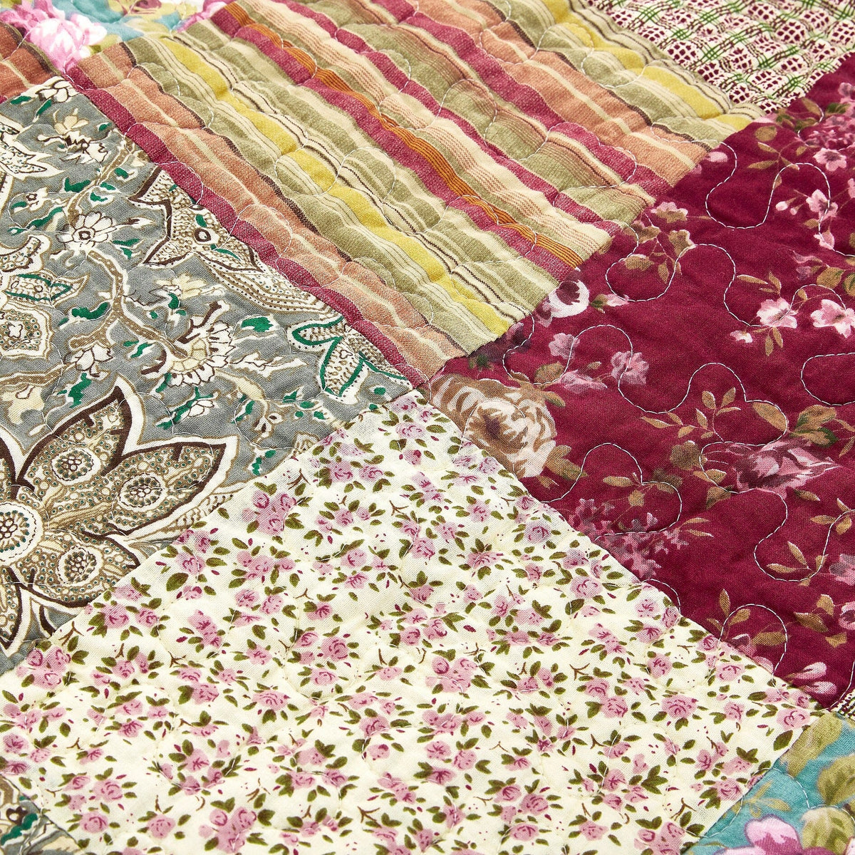 Close-up patchwork quilt with burgundy floral, teal medallion, and multicolor stripes.