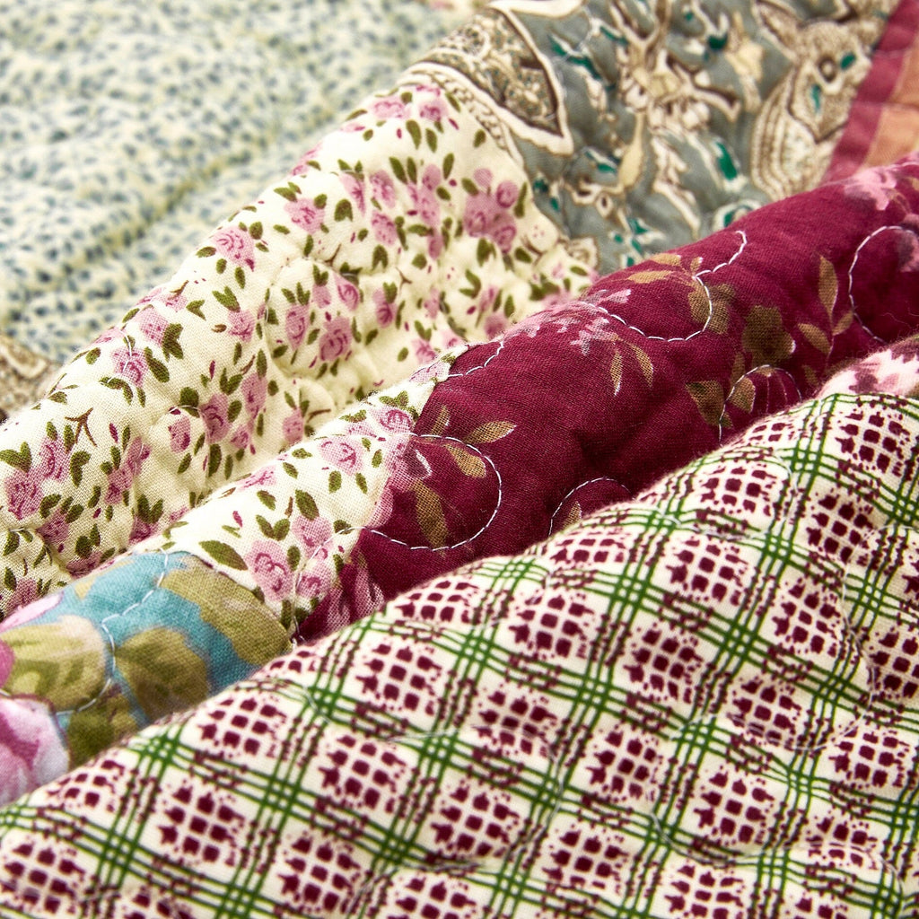 Close-up of quilted layers: burgundy, cream floral prints, and plaid stripe fabric.
