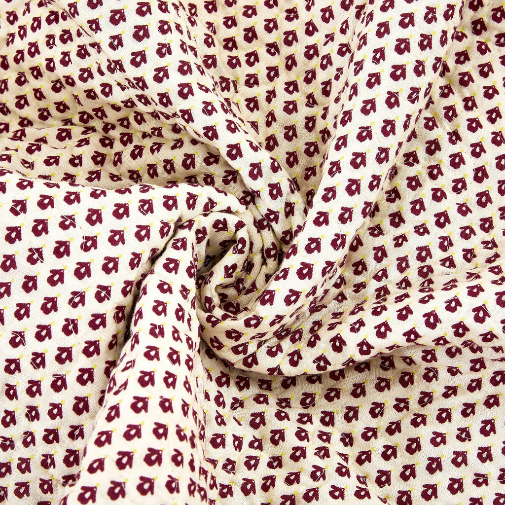 Close-up quilt section with repeating geometric motifs in burgundy and cream.
