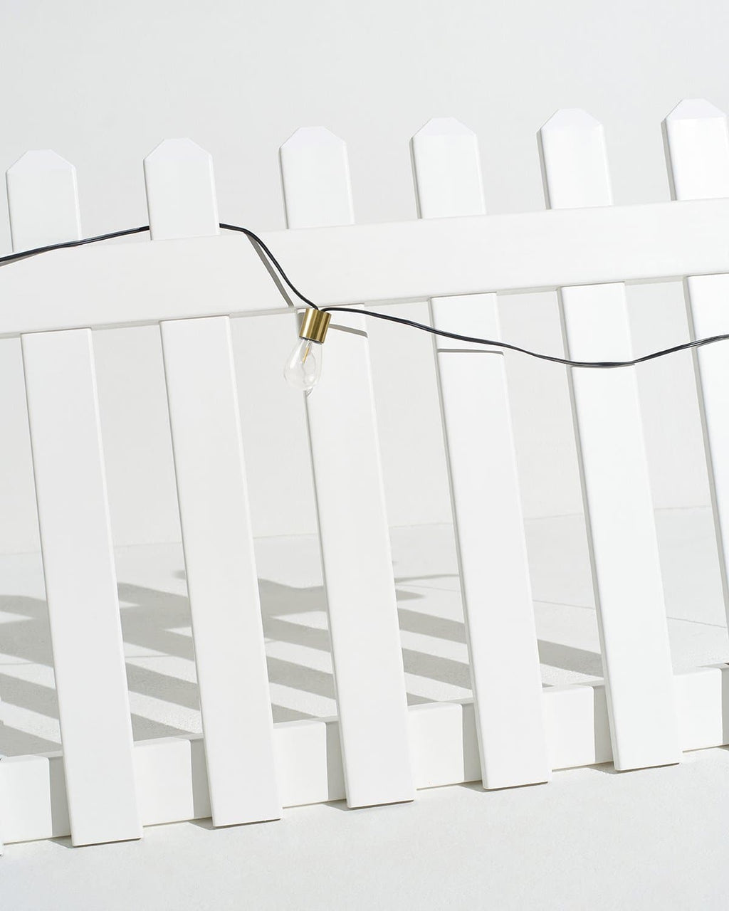 Solar string lights clipped across white fence pickets with clear bulbs on black wire