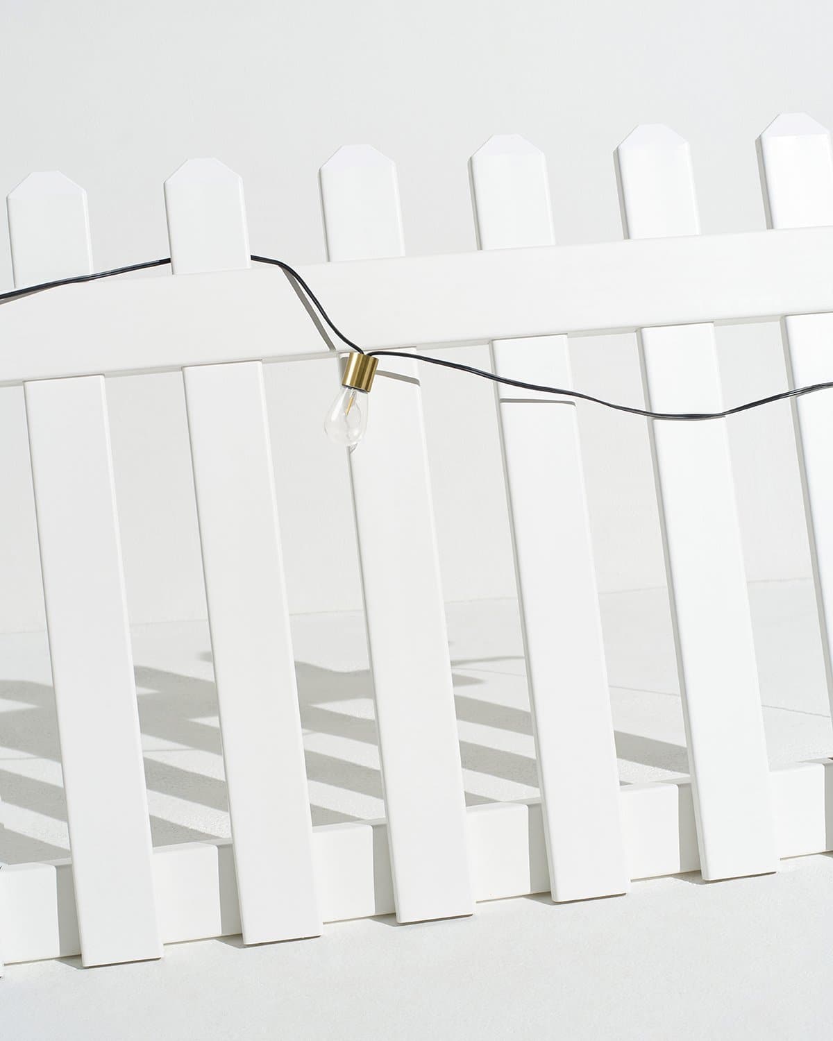 Solar string lights clipped across white fence pickets with clear bulbs on black wire