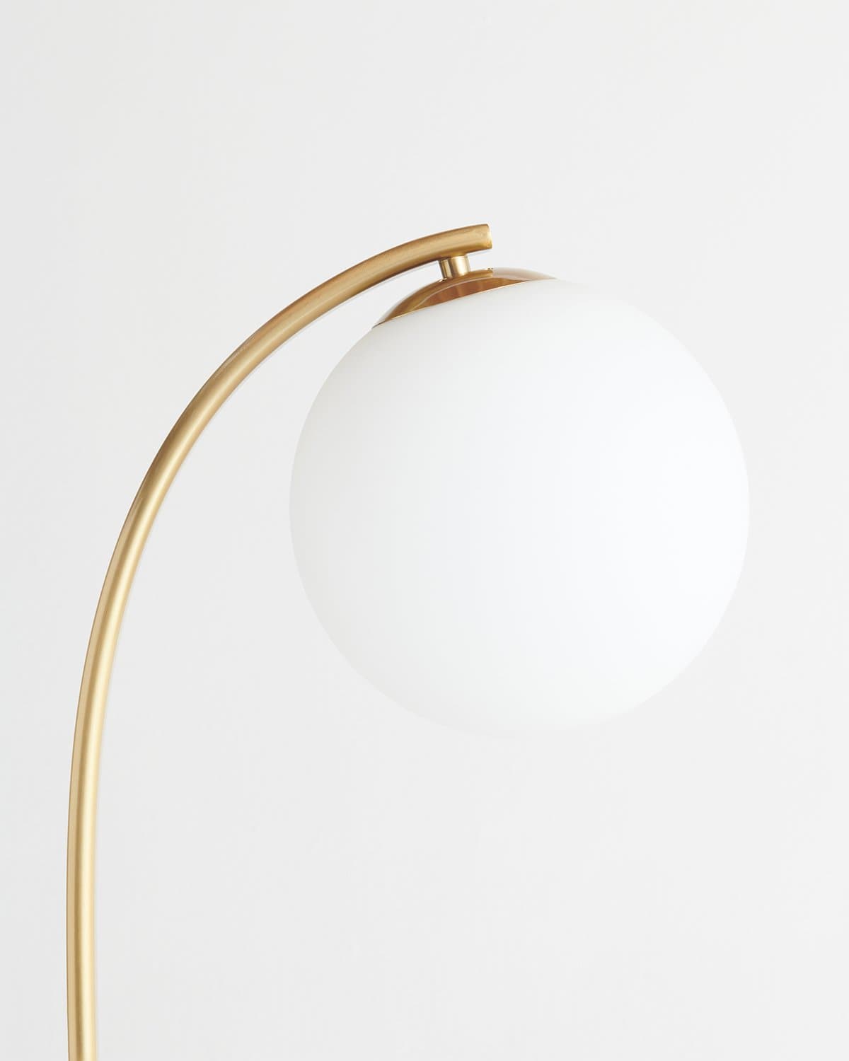 Close-up of gold arched floor lamp with white globe shade