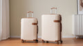 Two cream hard-shell suitcases with telescoping handles and spinner wheels