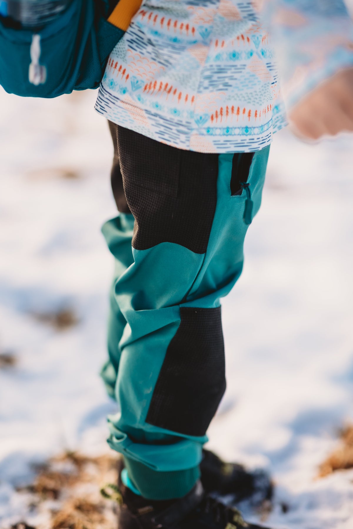 Water-resistant hiking pants in teal with dark panels, elastic cuffs and drawstring waist