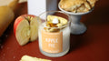 Apple pie container candle in clear glass jar with “APPLE PIE” label and wax topping