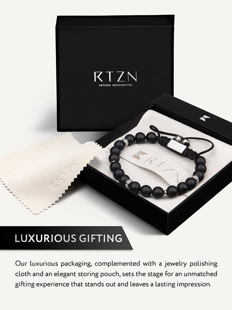 Black beaded bracelet laid in a gift box with rectangular metal charm and cord