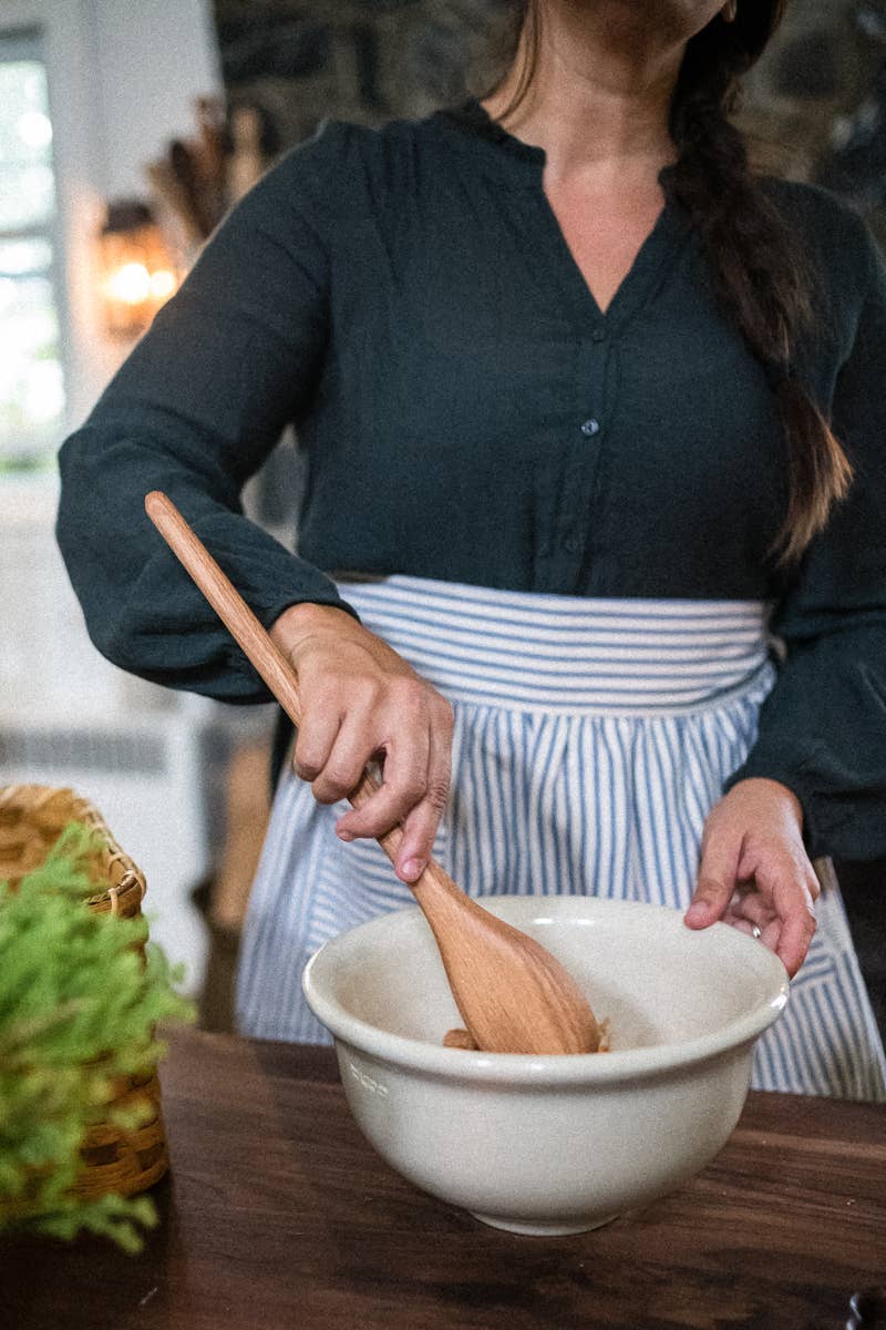Wooden spoon being used to stir in a white bowl, with long oval bowl.
