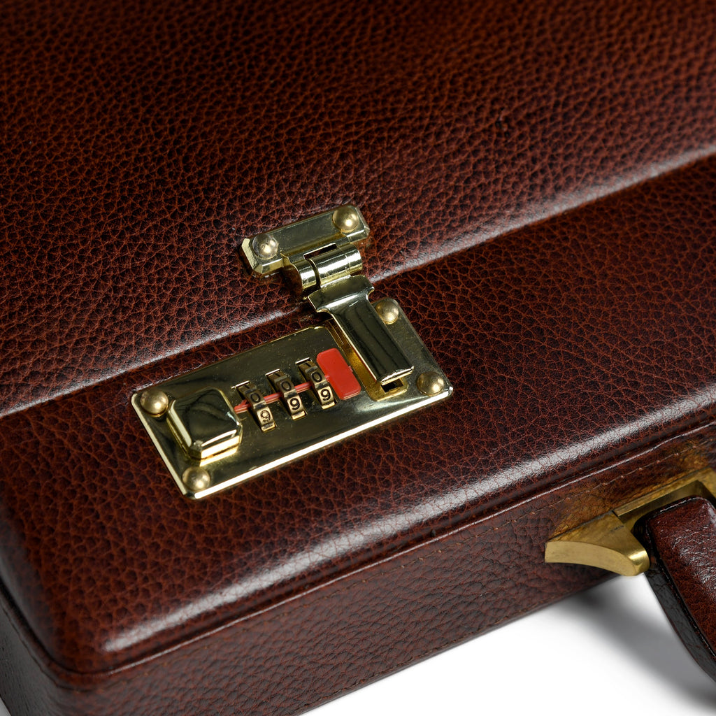 Close-up of brass combination lock on rich brown leather suitcase panel
