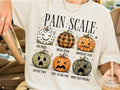 Cream graphic tee with pain scale pumpkins, including quotes like “No pain” and “Mild pain”
