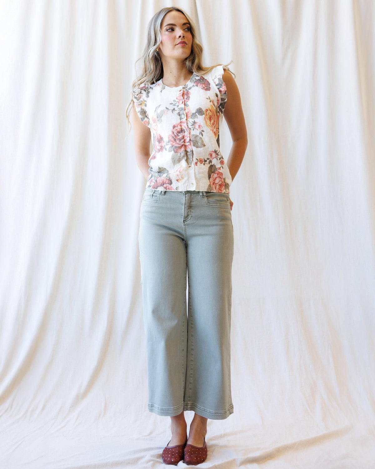 Cream floral sleeveless cardigan with button front, ruffled shoulders, ribbed waist