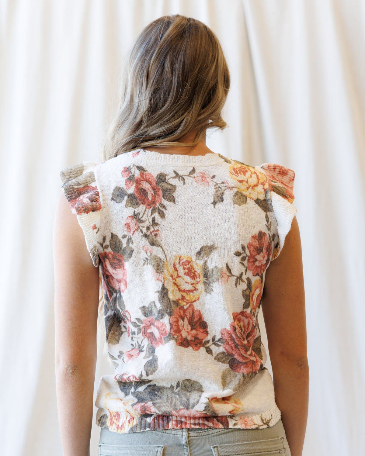 Cream floral sleeveless cardigan from back view with buttoned yoke and ribbed hem