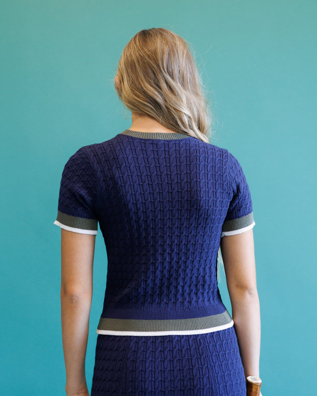 Back view: dark blue cable-knit crewneck sweater with short sleeves and stripe rib hem