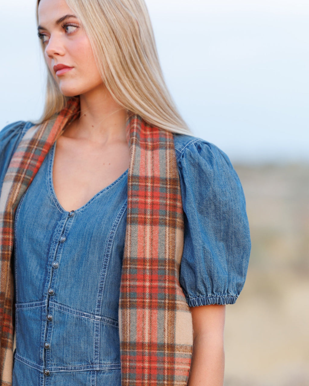 Plaid scarf worn draped at the neck, beige rust teal tones with fringed edge