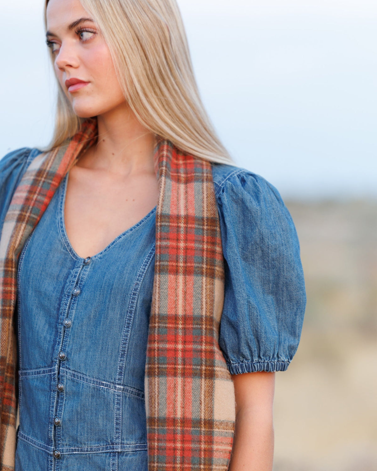 Plaid scarf worn draped at the neck, beige rust teal tones with fringed edge