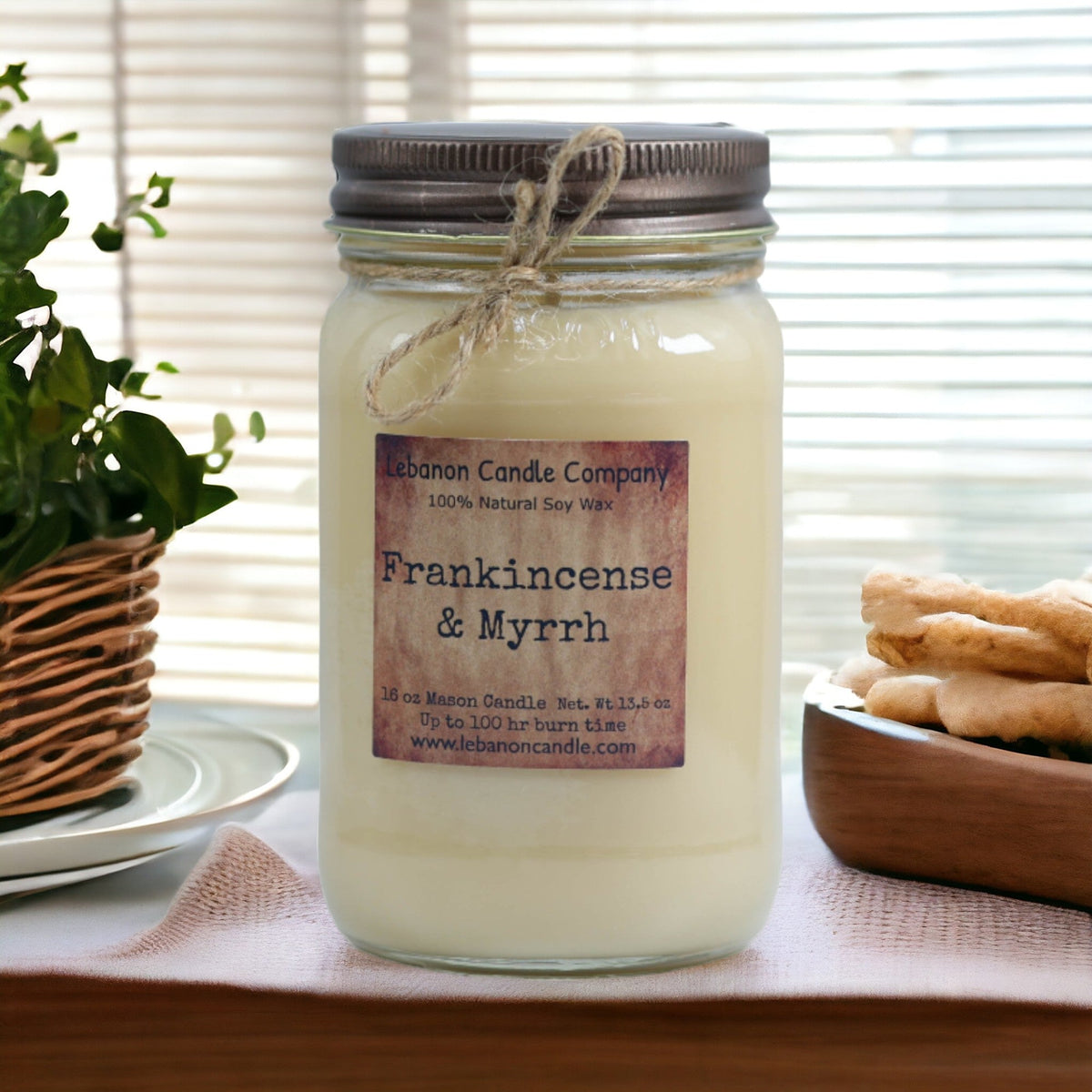 Soy candle jar with twine bow, Frankincense & Myrrh label, on fabric-covered tray