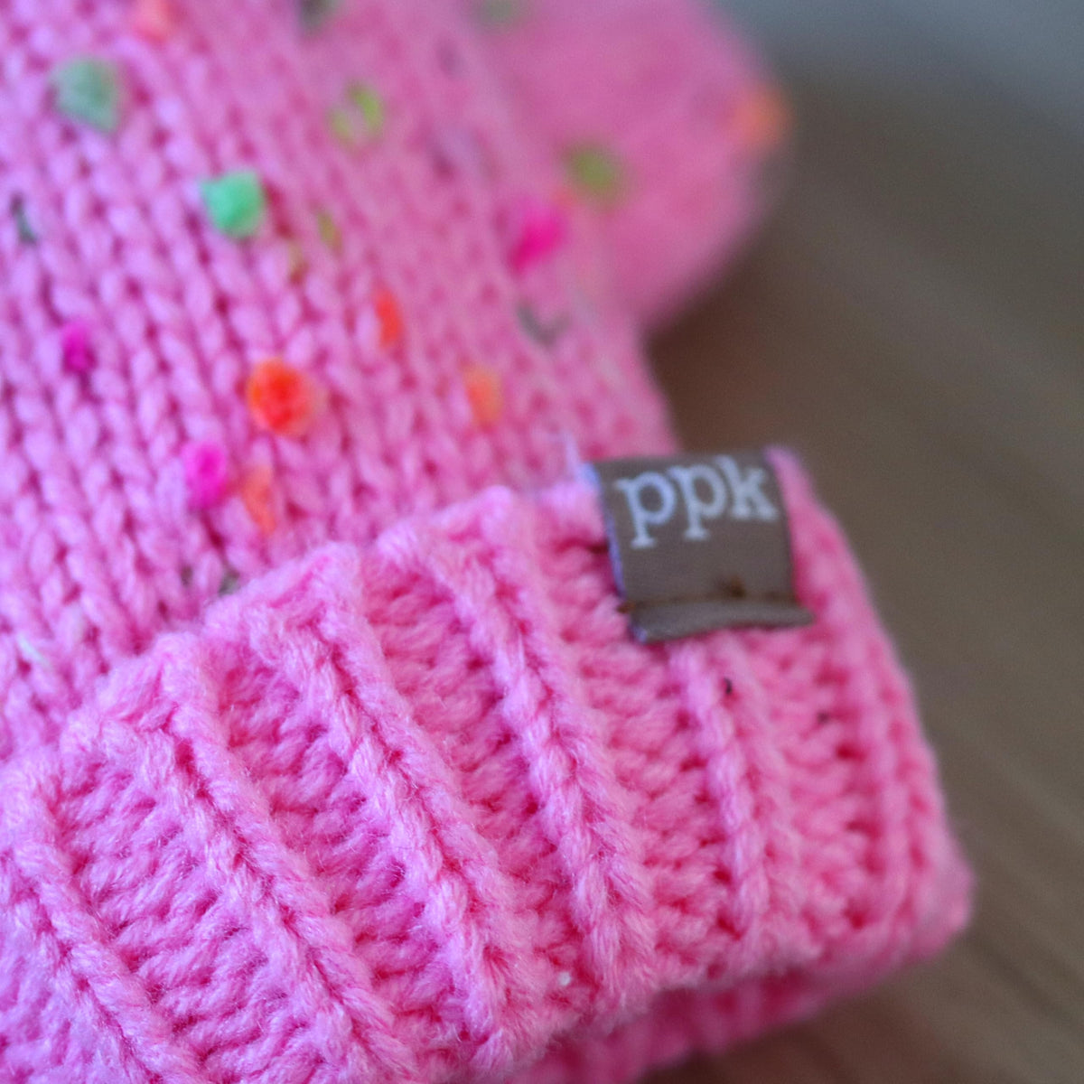 Pink speckled knit mitten cuff close-up with small fabric brand tag on the ribbed edge.