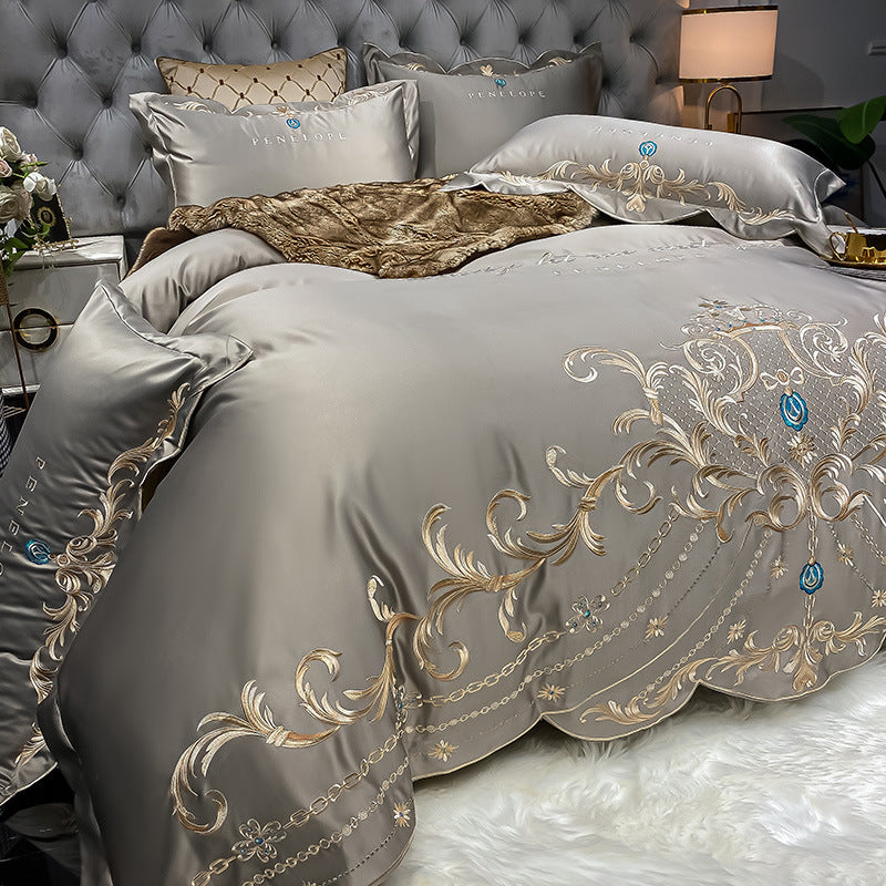 Light gray quilted bed sheet set with gold and blue ornate embroidery and pillowcases