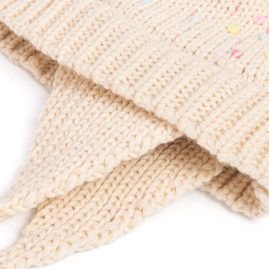 Off-white knit earflap beanie with ribbed texture and small speckled color dots.
