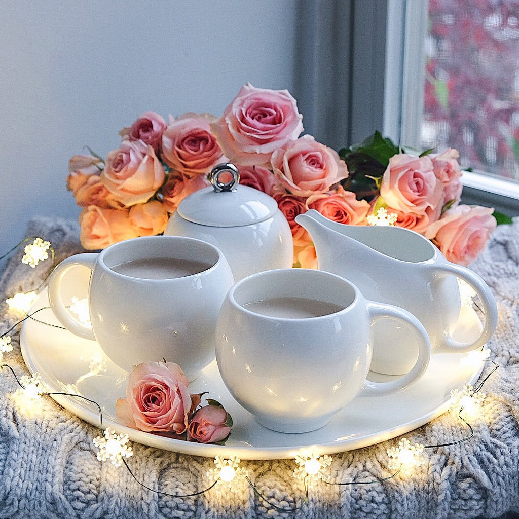 White ceramic teacups with curved handles arranged on a round serving tray