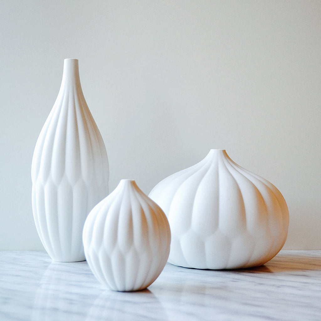 Group of four white porcelain vases with ribbed texture and fluted, bulbous necks