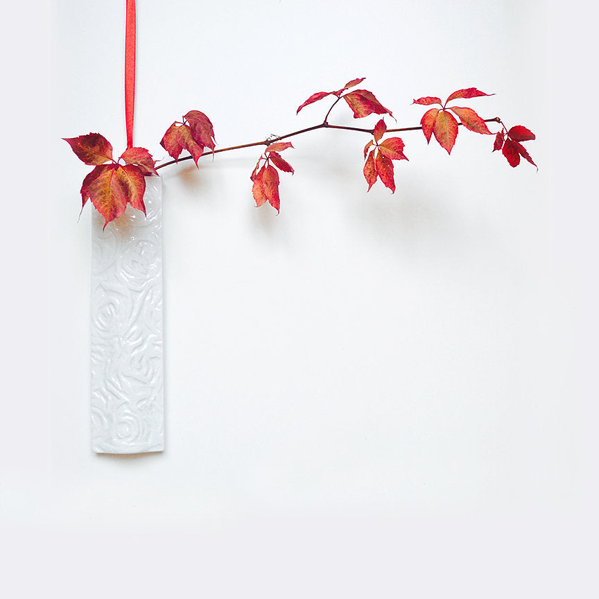Hanging wall vase with white embossed texture, holding red autumn leaves on stems
