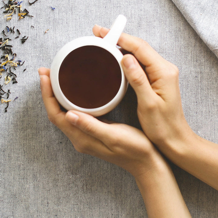 White ceramic teacup held in hands, filled with dark tea