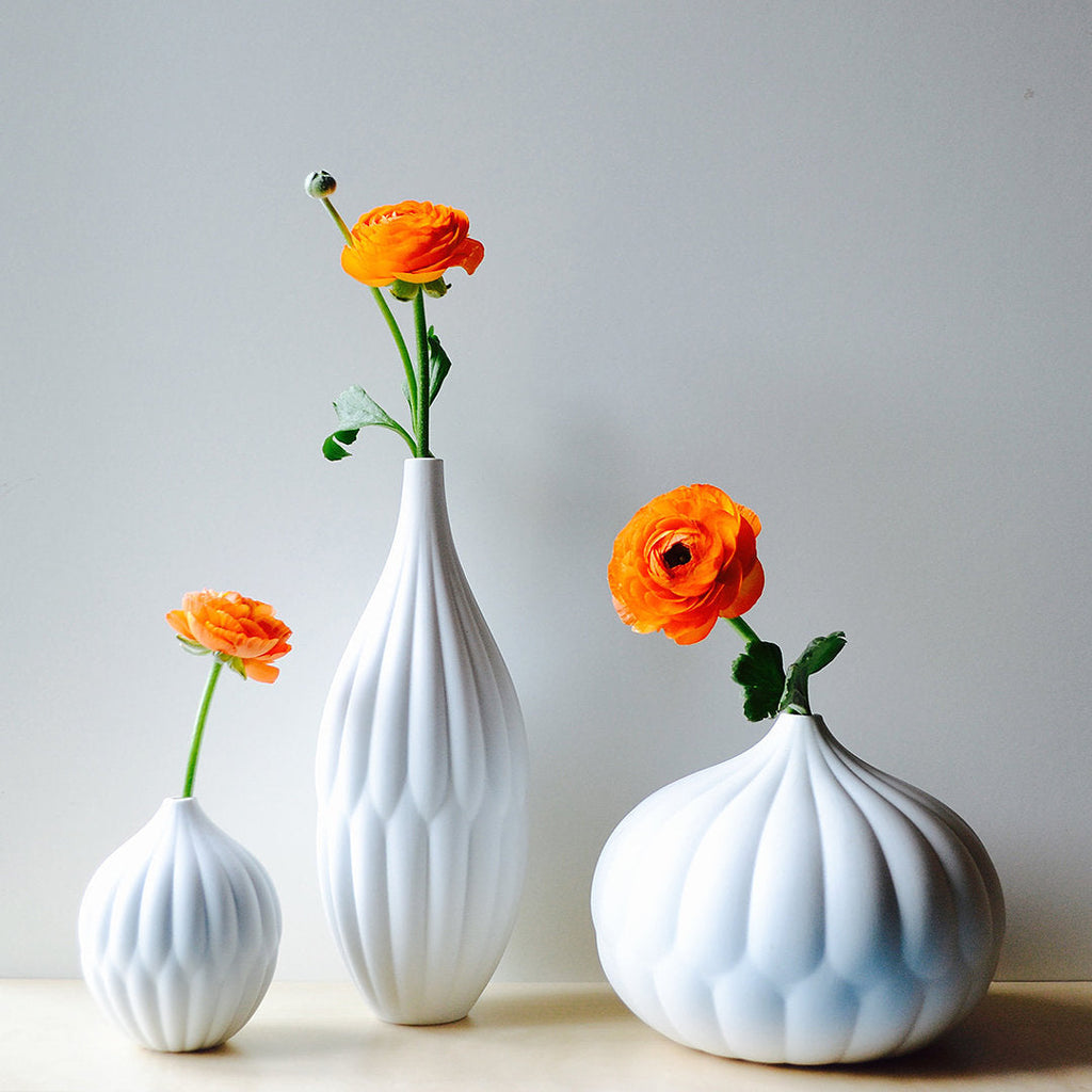 Three white porcelain vases with ribbed texture, bud vases holding orange flowers