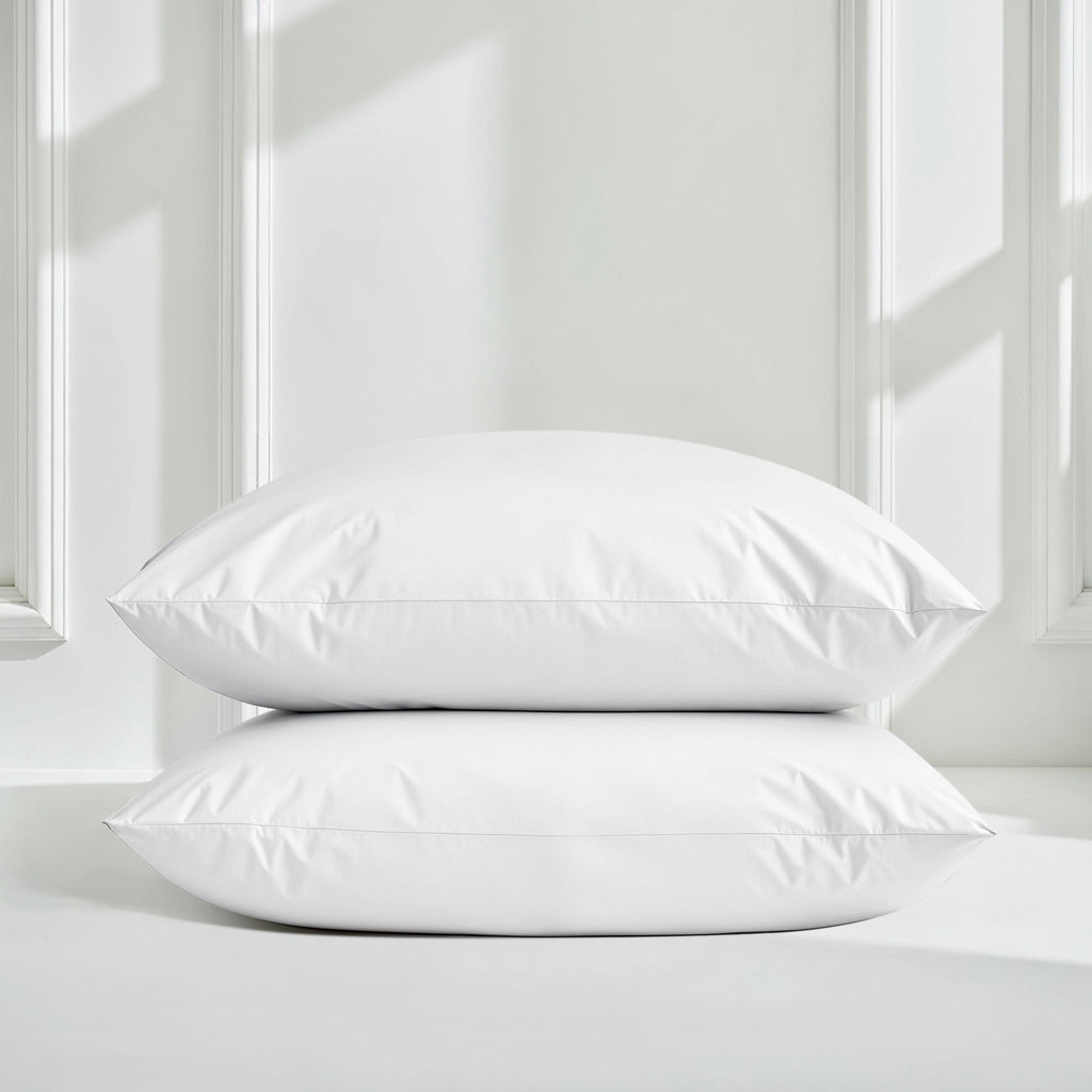 White sateen pillow shams stacked on a bed with matching duvet