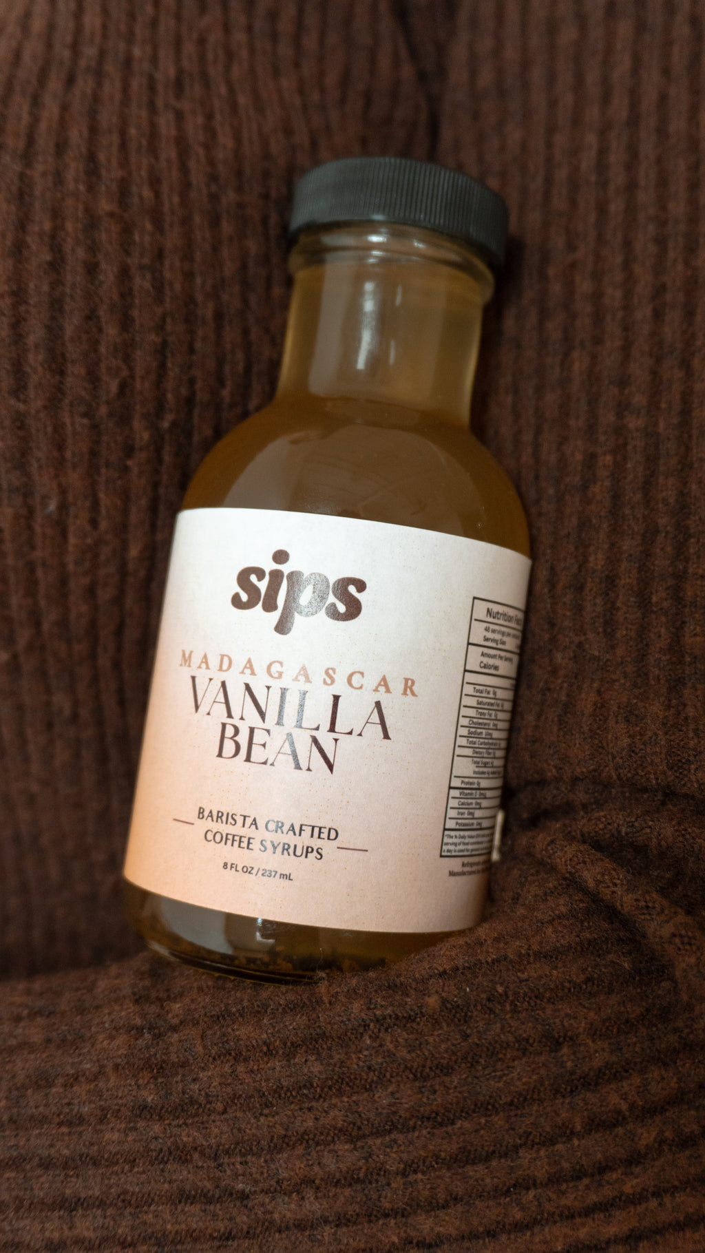 Vanilla bean coffee syrup bottle with Sips label and black cap on dark surface.
