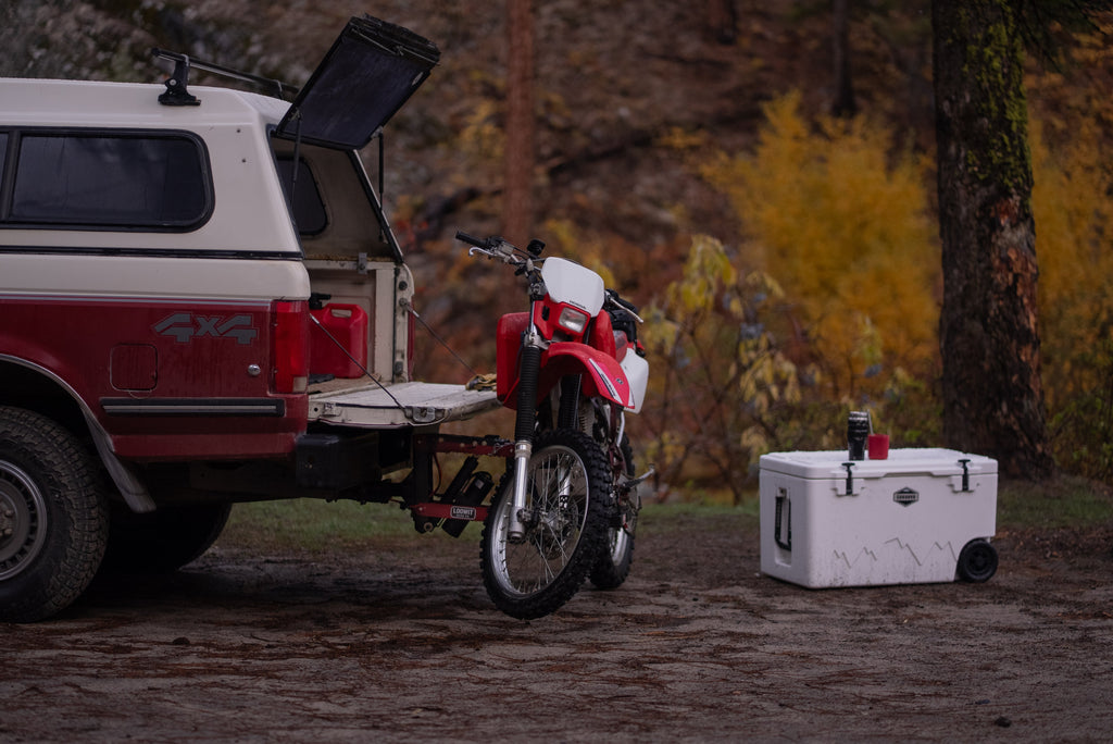 White 125 qt wheeled cooler with open lid outdoors, next to a red motorcycle