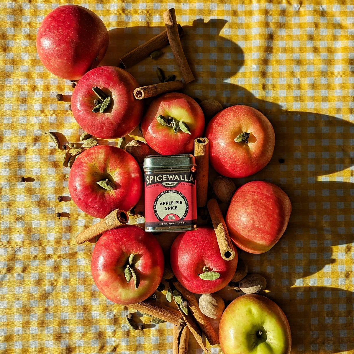 Spicewalla Apple Pie Spice tin centered among apples and cinnamon sticks