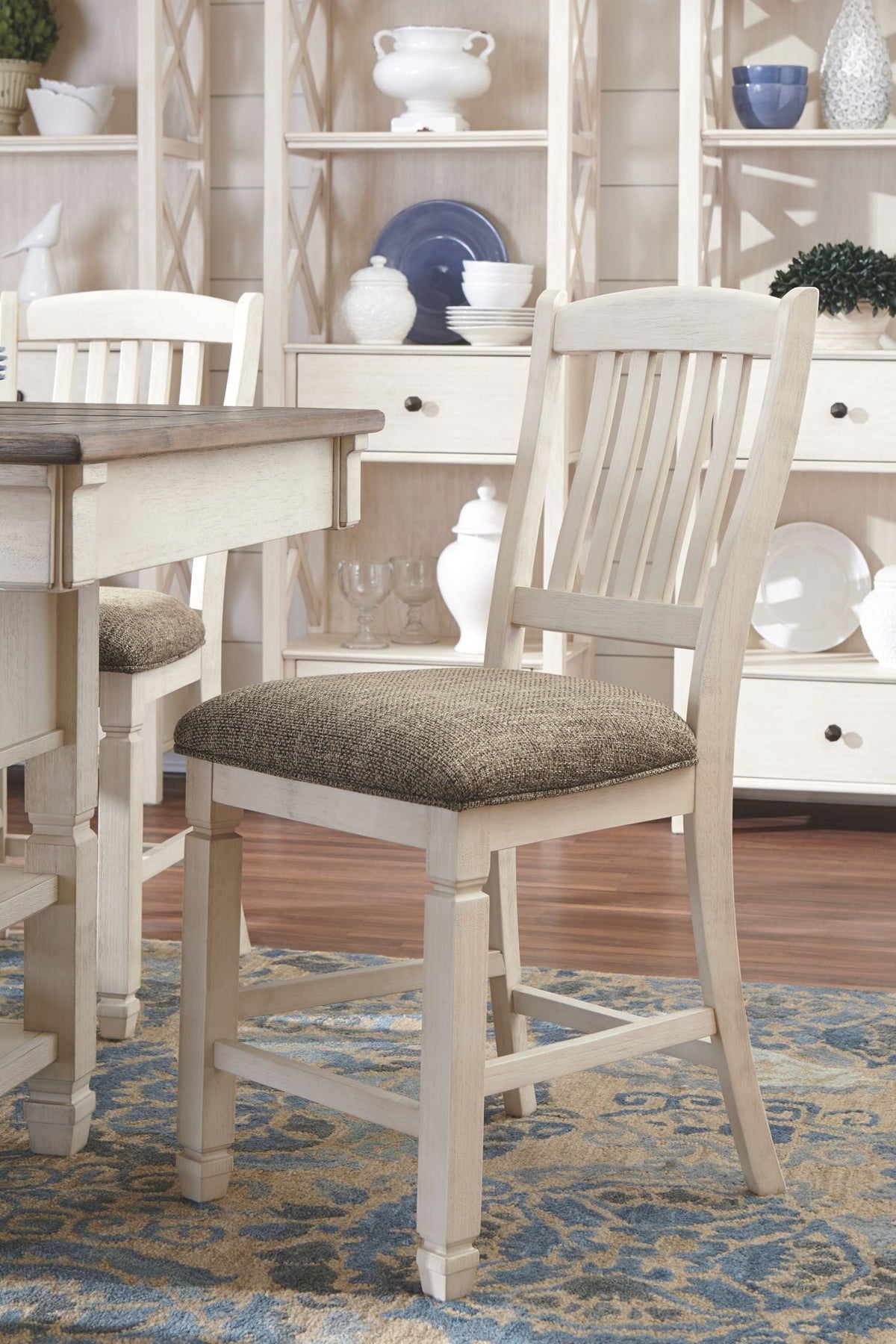 Cream dining chair with gray upholstered seat next to beige counter table and open shelving.