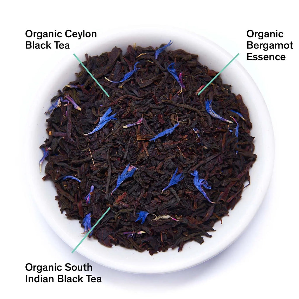 White bowl of dark black tea leaves with blue fragments, showing organic blend labels