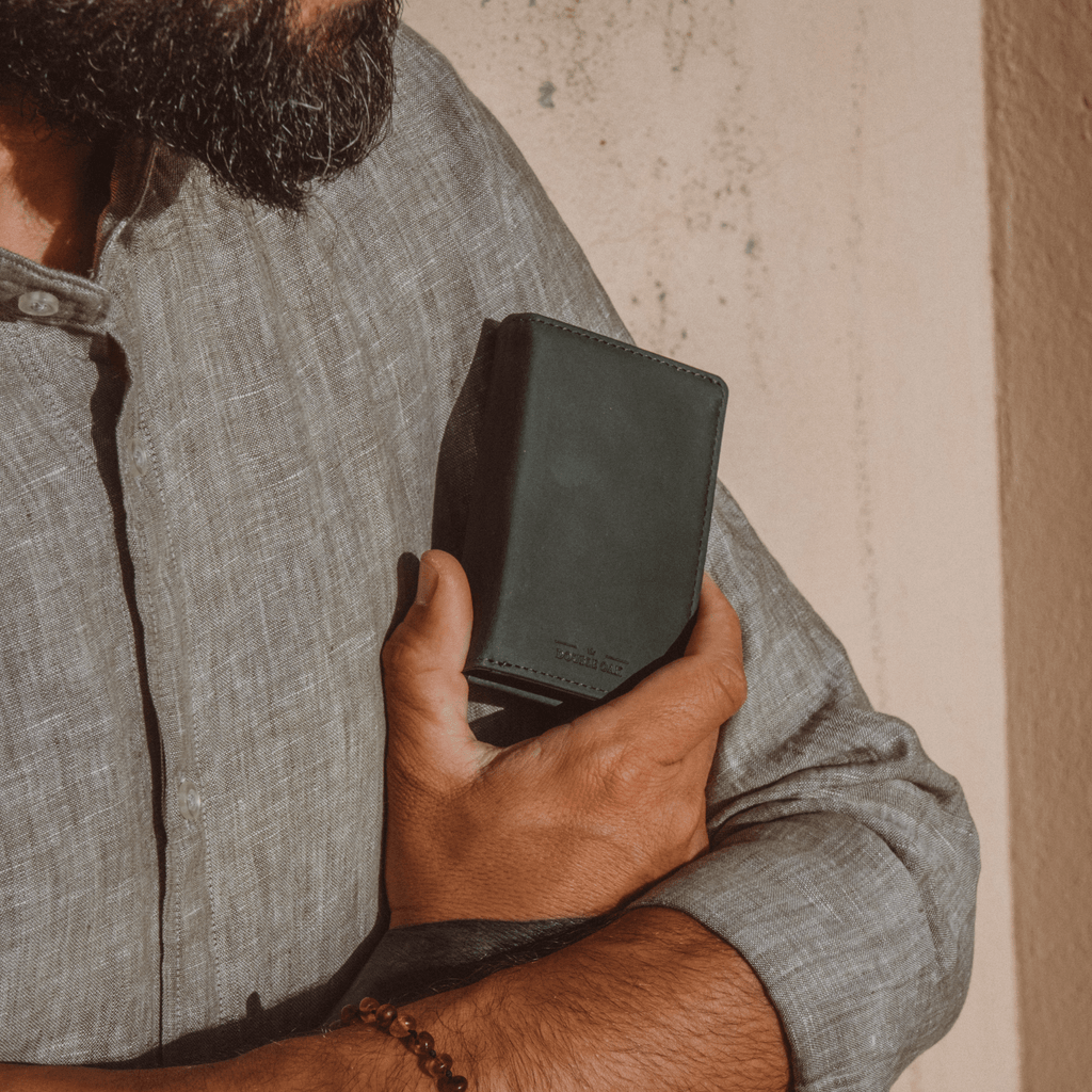Dark green bifold wallet in a man’s hand, stitched front with logo.