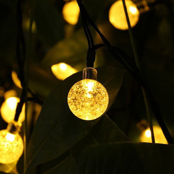 Close-up of outdoor solar fairy light globe bulb on black wire, warm white
