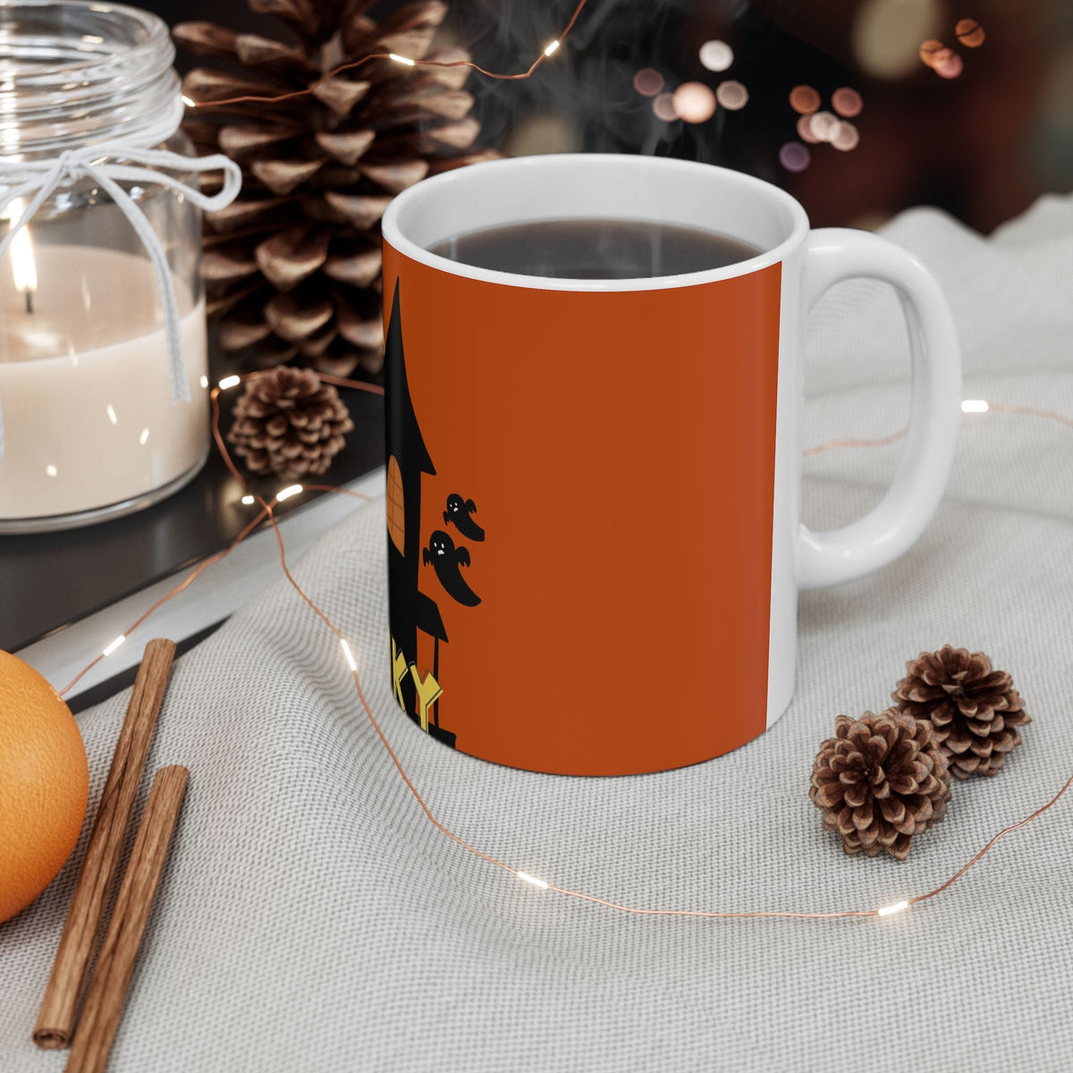 Orange ceramic coffee mug with black haunted house and bats graphic, white handle