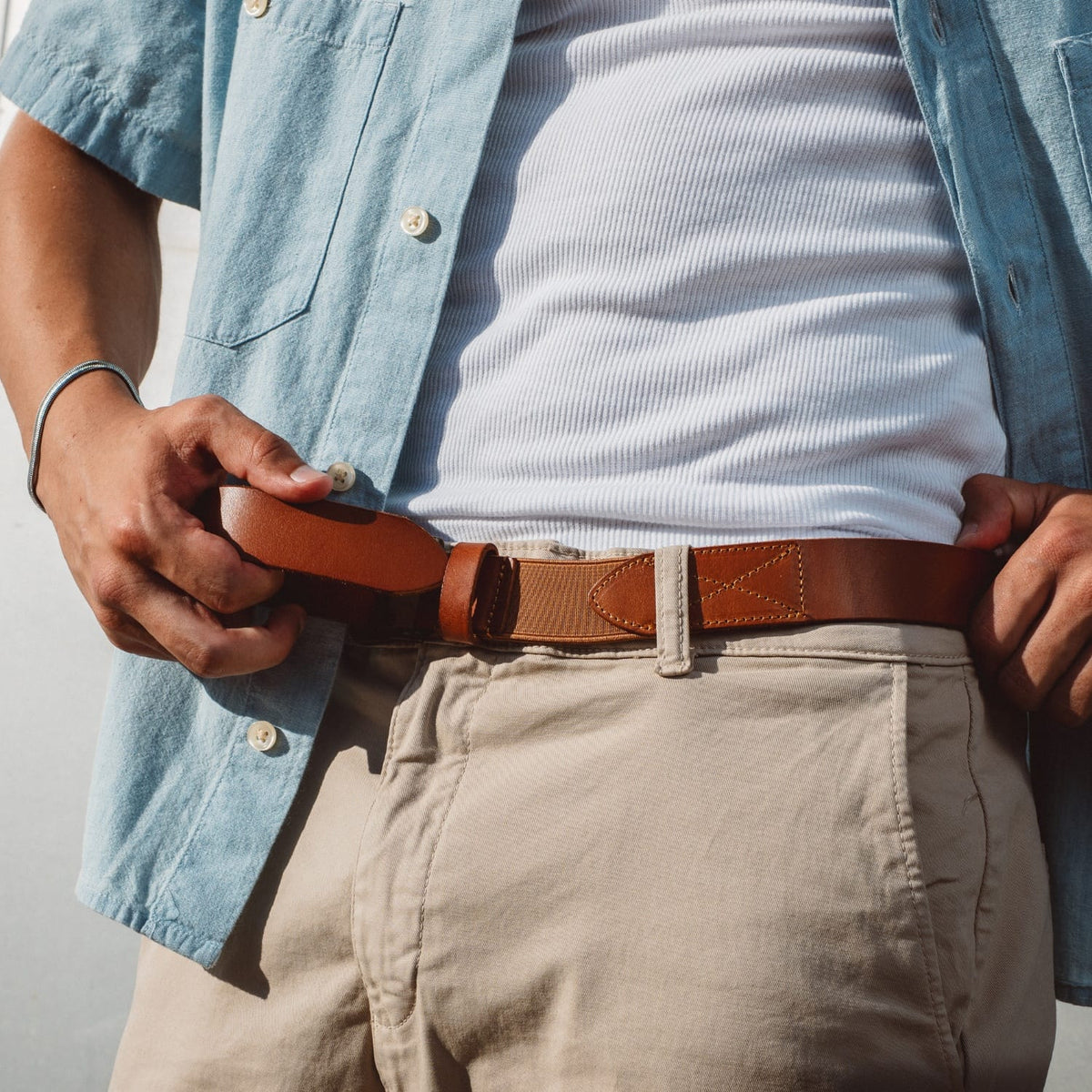 Brown leather stretch belt with square silver buckle, worn with trousers