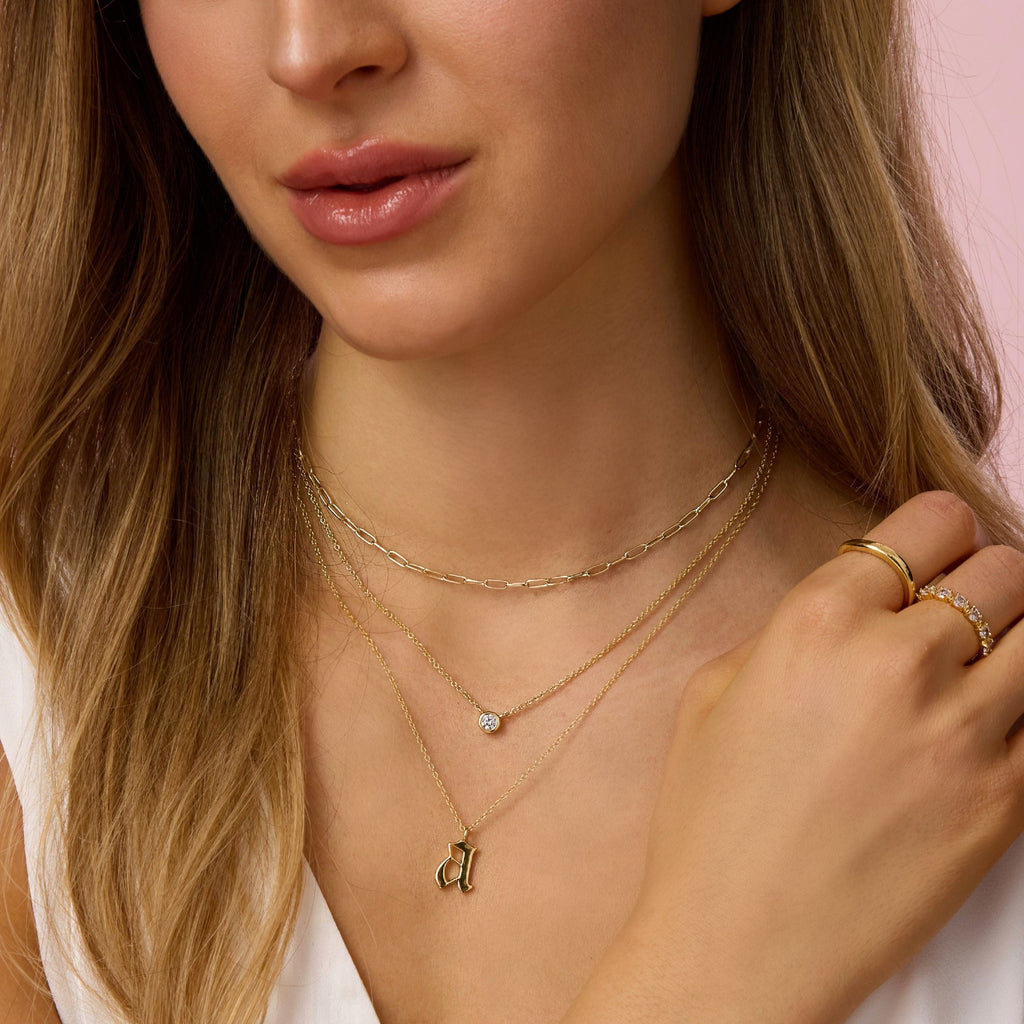 Gold chain necklace with round bezel-set diamond pendant at collar