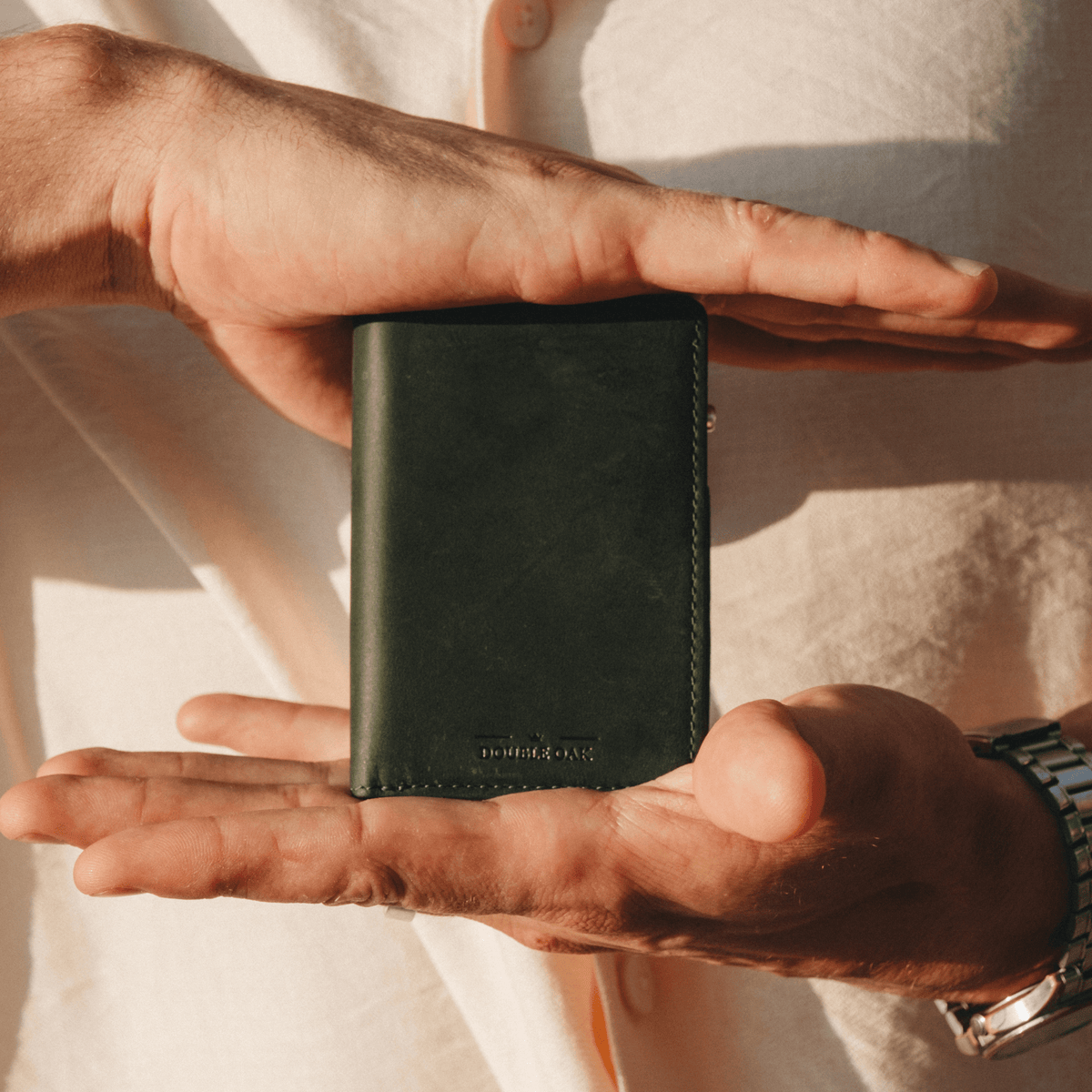 Dark green leather bifold wallet with stitched edges, held in hands