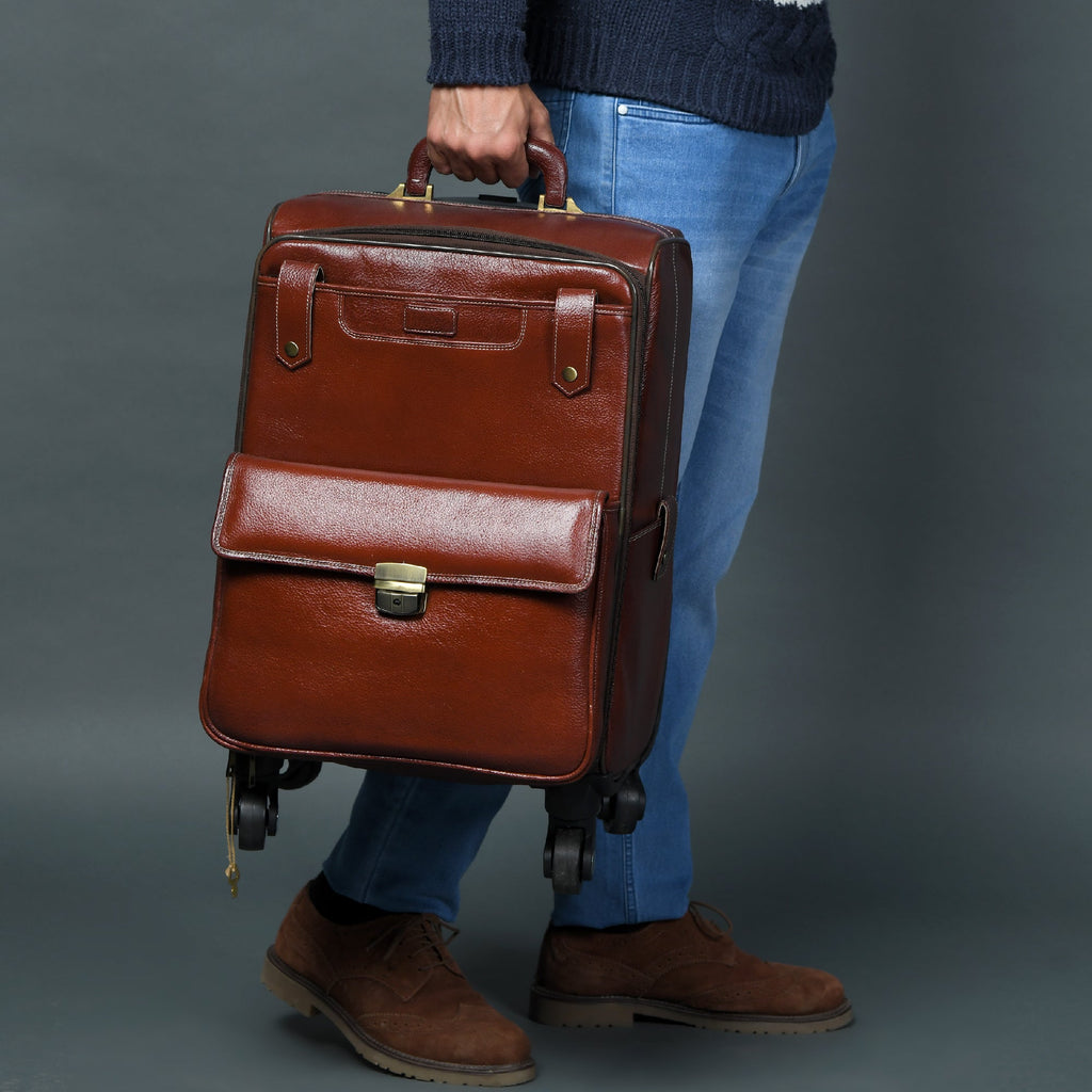 Brown leather carry-on trolley bag with front flap, buckle strap, and four rolling wheels