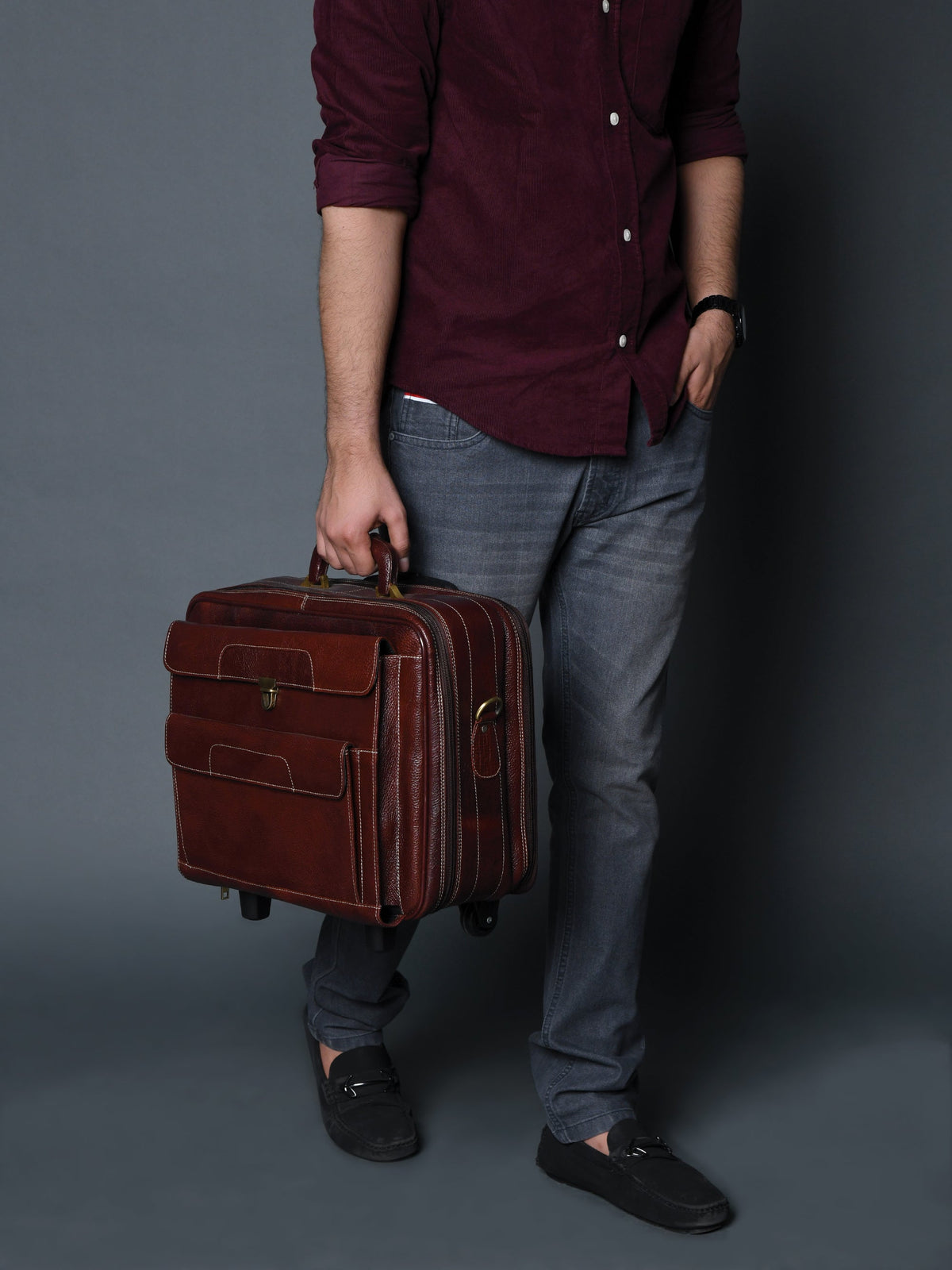 Brown leather trolley suitcase bag held by handle with front flap and four corner wheels